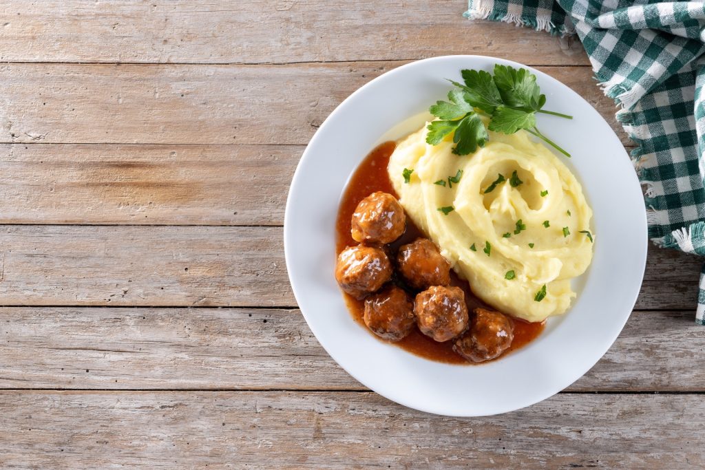 Köttbullar i sås med potatismos och persilja på en vit tallrik