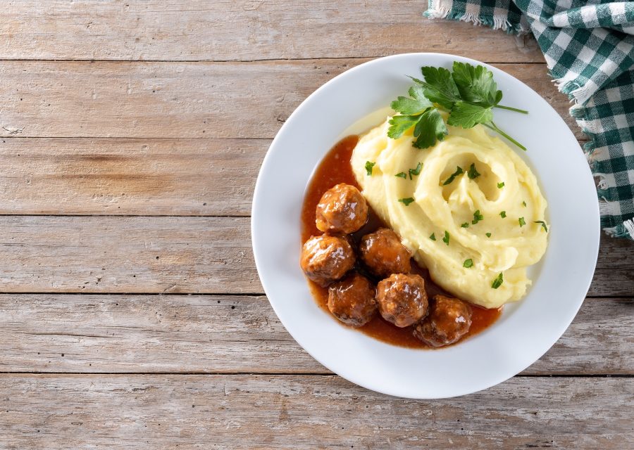 Köttbullar i sås med potatismos och persilja på en vit tallrik