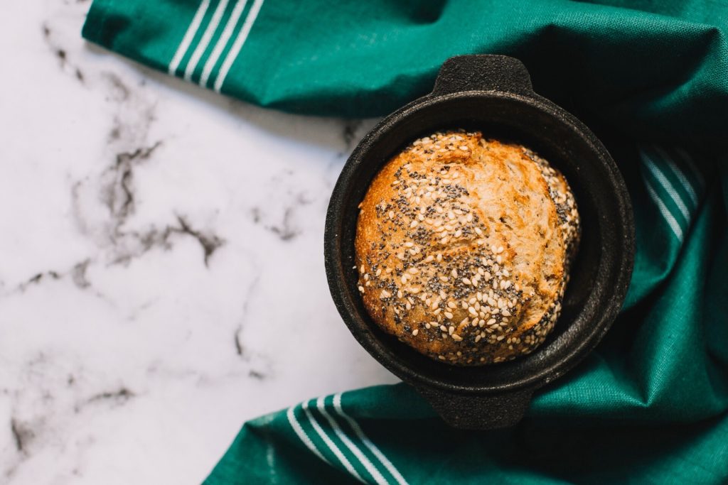 Nybakat grovt bröd med frön i en svart gjutjärnsgryta på marmorbord
