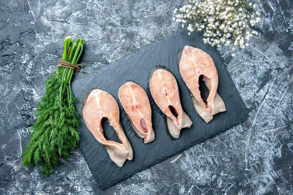 Råa fiskskivor på en svart skifferbricka bredvid en knippe färsk dill