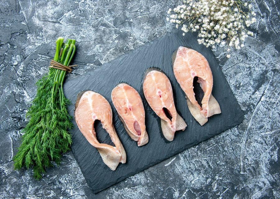Råa fiskskivor på en svart skifferbricka bredvid en knippe färsk dill