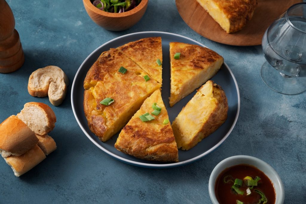 Spansk potatisomelett skuren i bitar på en tallrik bredvid bröd
