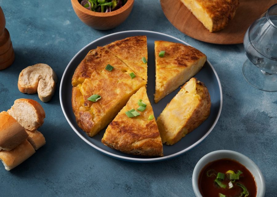 Spansk potatisomelett skuren i bitar på en tallrik bredvid bröd